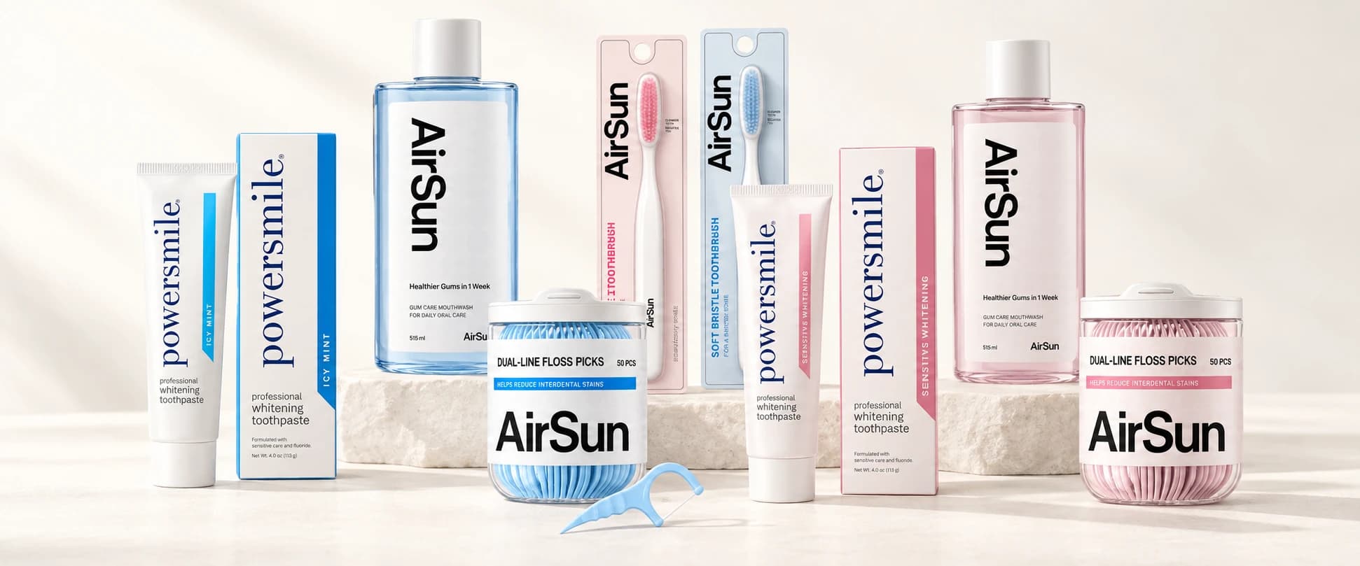 Blue and pale pink toothpaste, mouthwash, toothbrushes and floss picks arranged together on an ivory display.