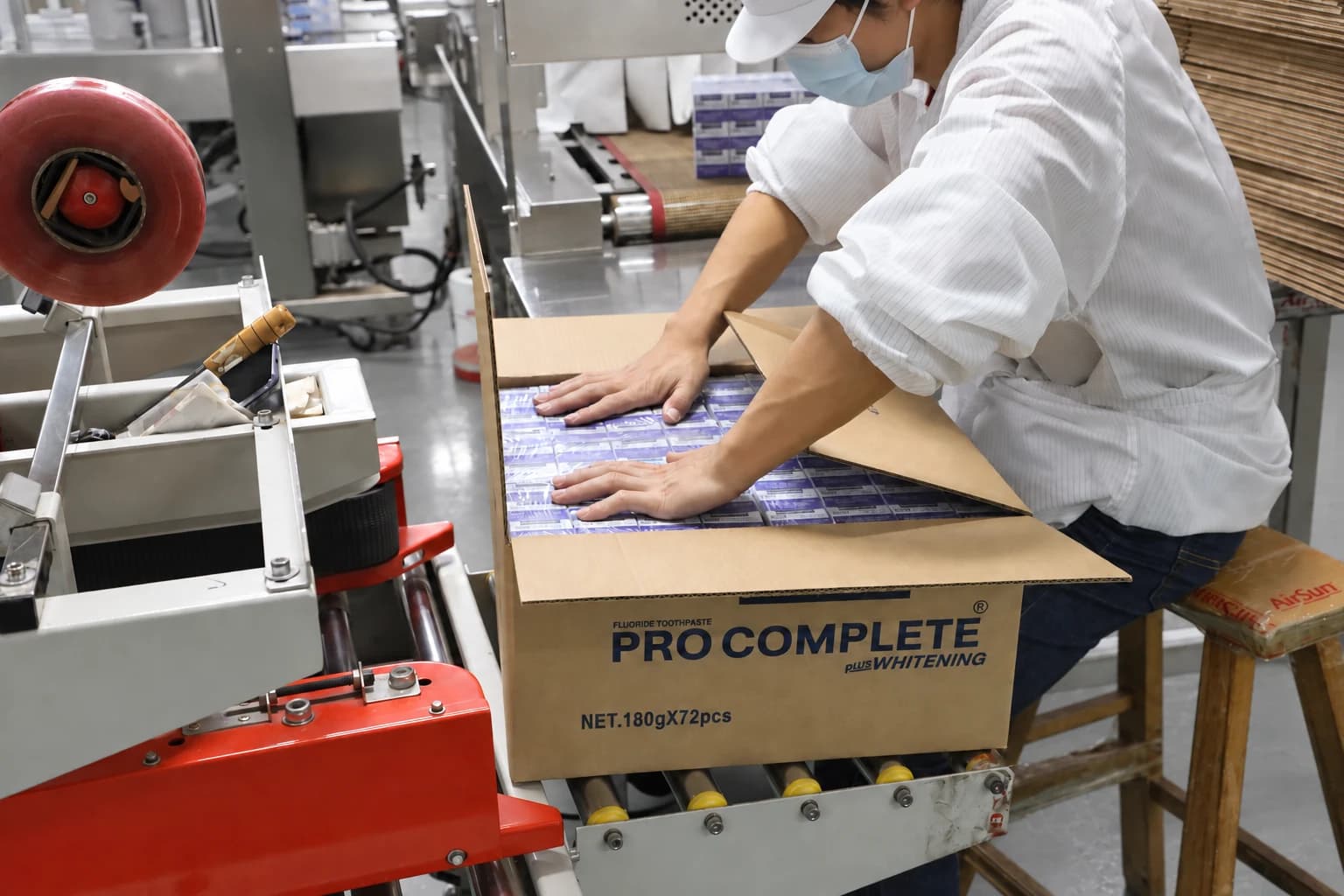 An Airsun operator arranging toothpaste cartons inside a shipping case beside packing equipment.